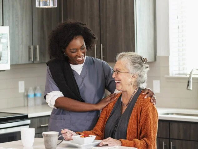 senior woman smiles at her home care nurse while enjoying lunch in the kitchen