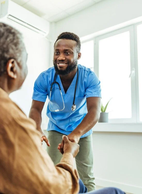 senior man smiles up at his caregiver, who is reaching down to help him stand