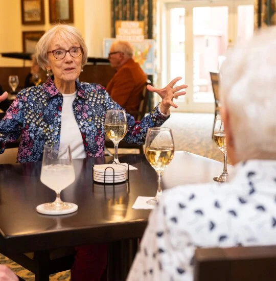 two senior women enjoy wine together at a lounge in Claridge Court Senior Living Community