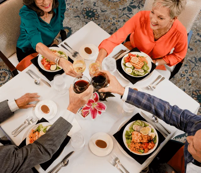 Four people toast with wine glasses at a dining table set for lunch.
