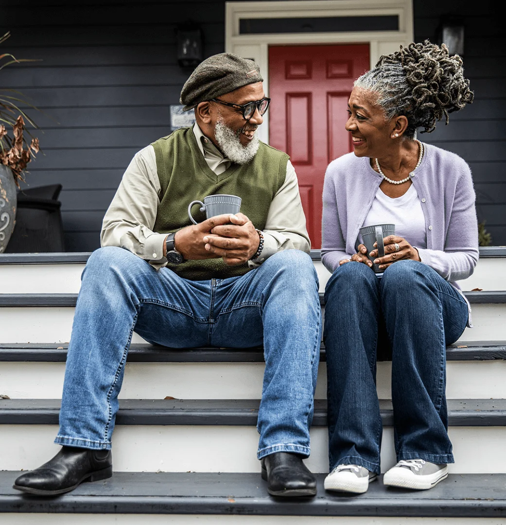 A couple sits on steps outside their home, enjoying coffee and conversation.