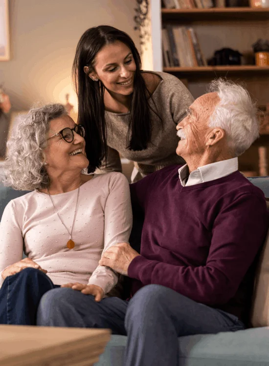 Three people share laughter and connection on a cozy couch indoors.