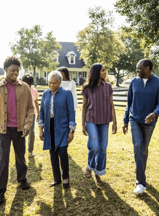 A family walks together on grass near a house under sunny skies.