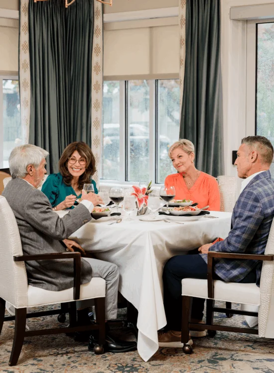 Four people enjoy a meal at an elegant dining table with wine glasses and flowers.