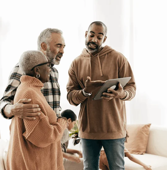 Three people gather around looking at tablet together indoors.