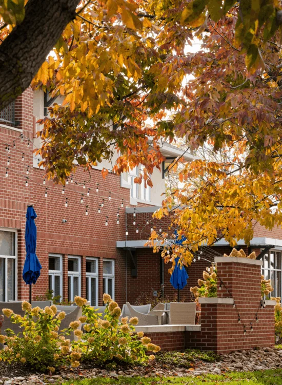 Autumn leaves frame brick building with string lights and outdoor seating area.