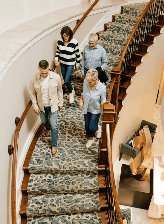 Four adults walk down patterned carpet stairs indoors.
