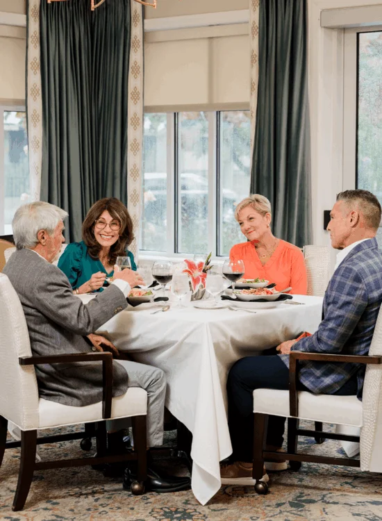 Four people enjoy a meal at an elegant dining table with wine glasses and flowers on it.