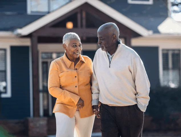 A couple walks hand-in-hand outside their home on a sunny day.