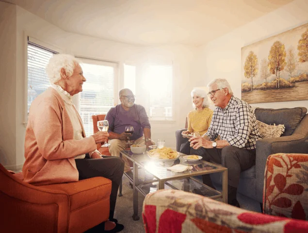 Four older adults enjoy snacks and drinks together indoors with warm lighting.