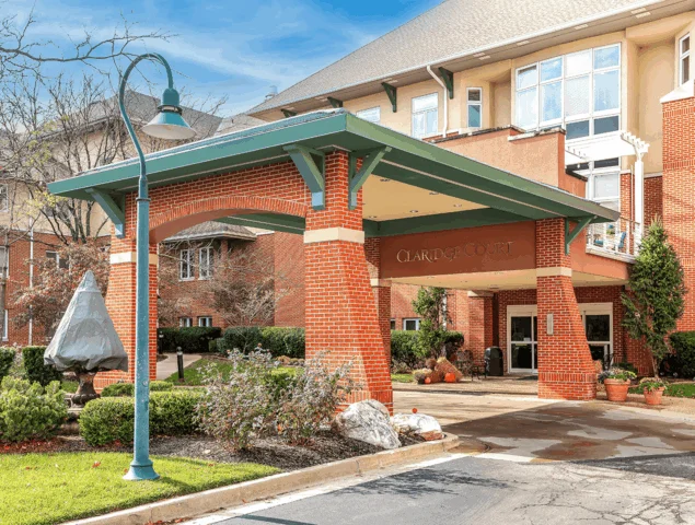 Entrance to Claridge Court with brick pillars and green awning under blue sky.