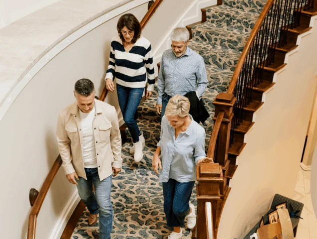 Four people descend a staircase with patterned carpet and wooden railings.