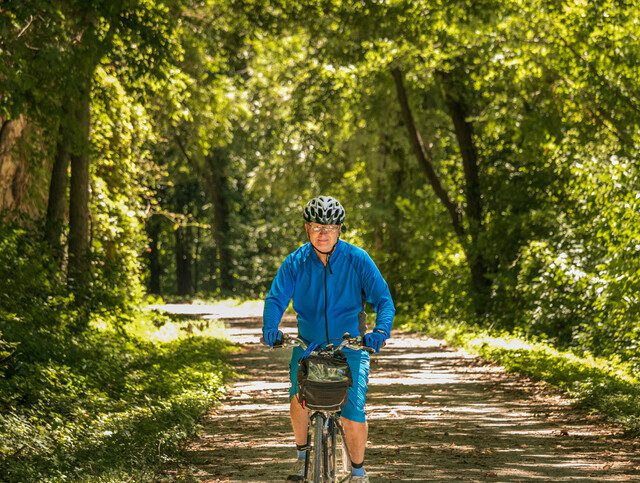 Senior man bicyclist in blue jersey riding on Midwestern trail in summer
