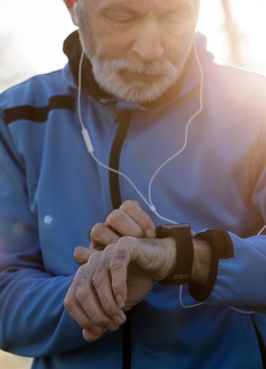 senior man wearing athletic clothes and headphones checks his smart watch after a run