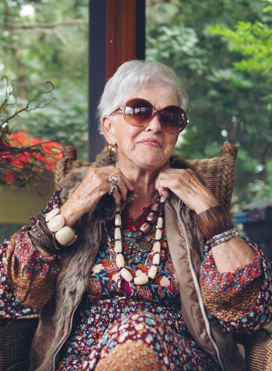 well-dressed senior woman places her hands on her necklace to show off her accessories