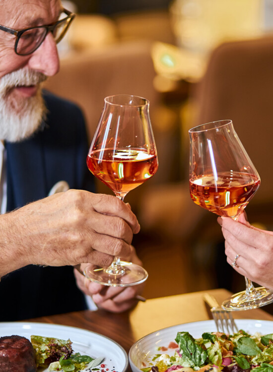 senior couple toasts glasses of wine together over an elegant, upscale meal