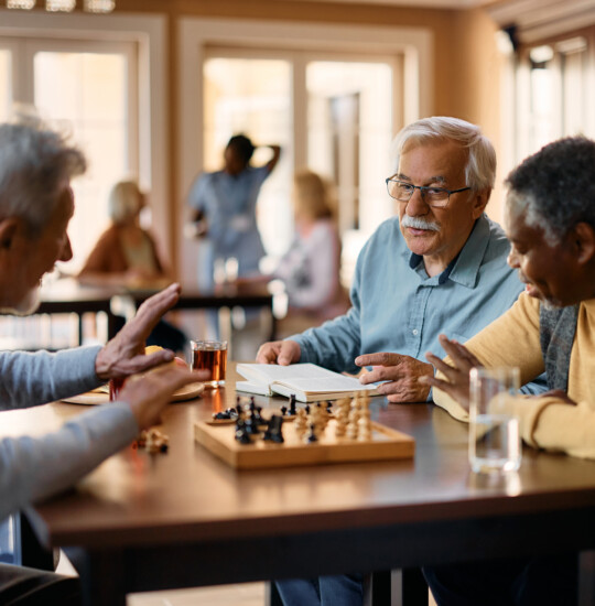 group of senior friends discuss chess moves during a game at their senior living community