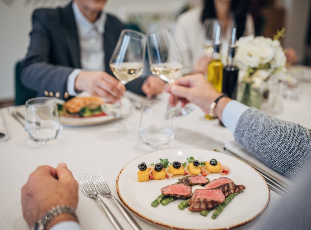 seniors toast wine glasses together over steak dinner in formal dining venue