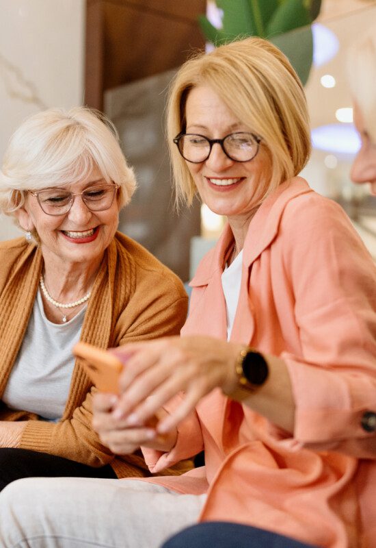group of senior women smile and browse through a phone together while seated