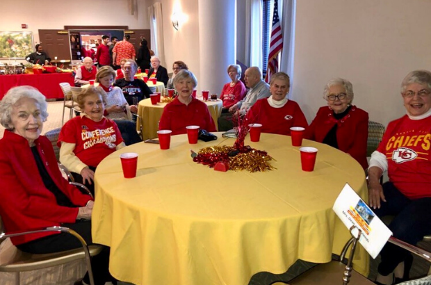 Claridge Court Senior Living Community residents smile for a photo, seated at a table during a Superbowl party