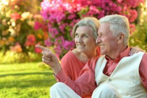 happy senior couple sits on the grass in the garden smiling, the senior man pointing at something in the distance