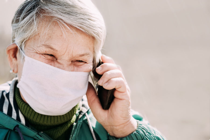 elderly woman talking on the phone while wearing a face mask