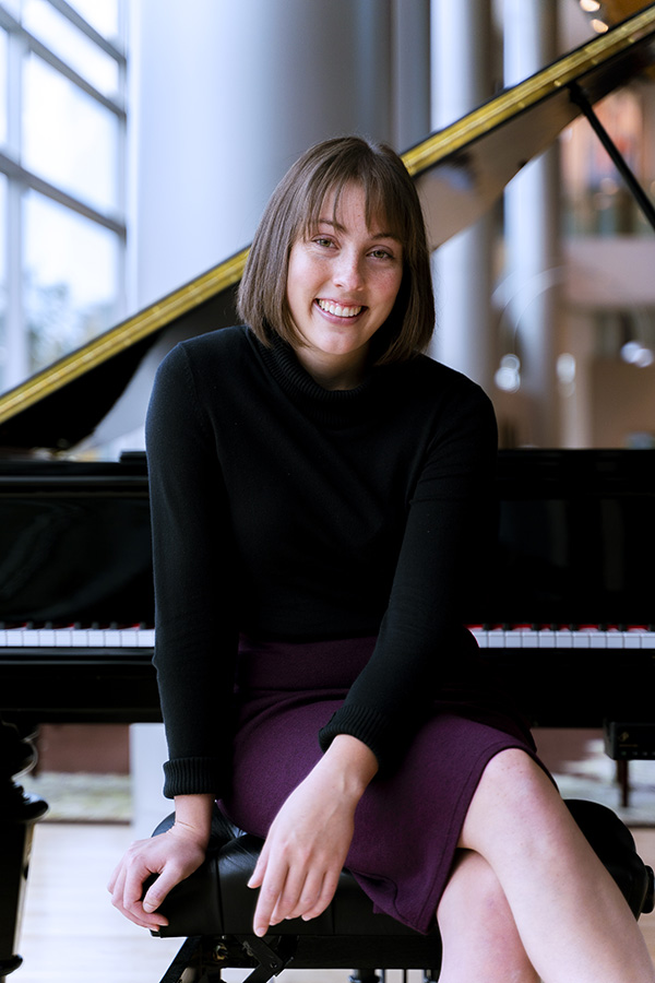 25 year old music student Beth Christensen sits in front of a grand piano at Claridge Court Senior Living Community, smiling