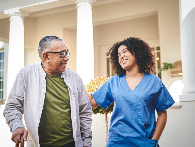 senior man and his female caregiver smile while on a scenic walk outside of Claridge Court Senior Living Community