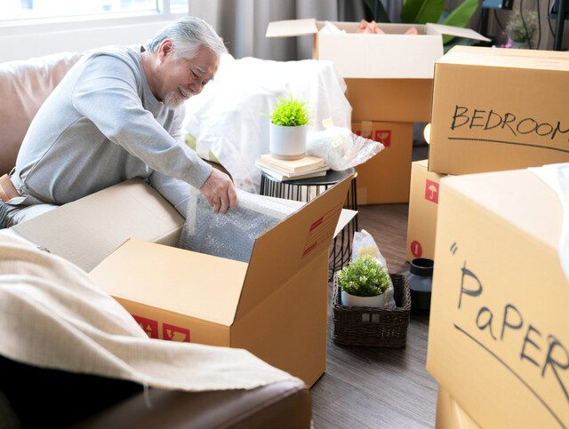 senior man sorts his belongings in boxes, downsizing for a move to a senior living community