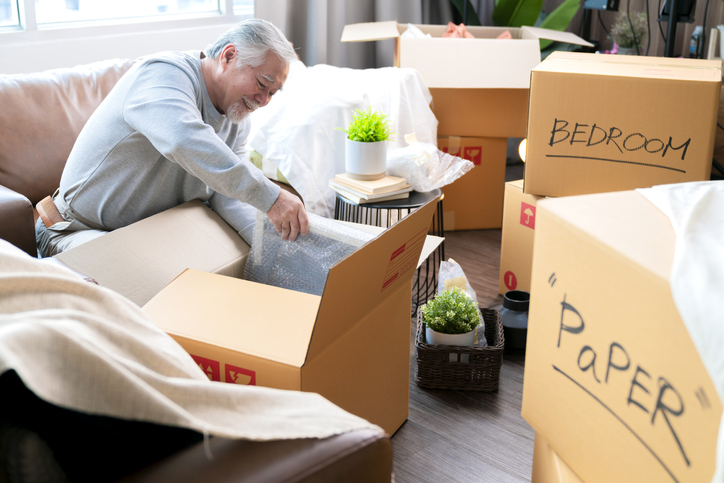 senior man sorts his belongings in boxes, downsizing for a move to a senior living community