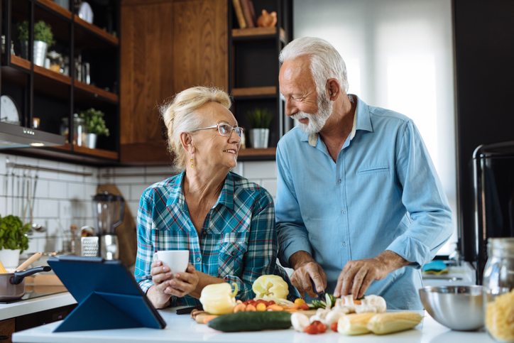 senior couple looks lovingly at one another while preparing a meal in their kitchen