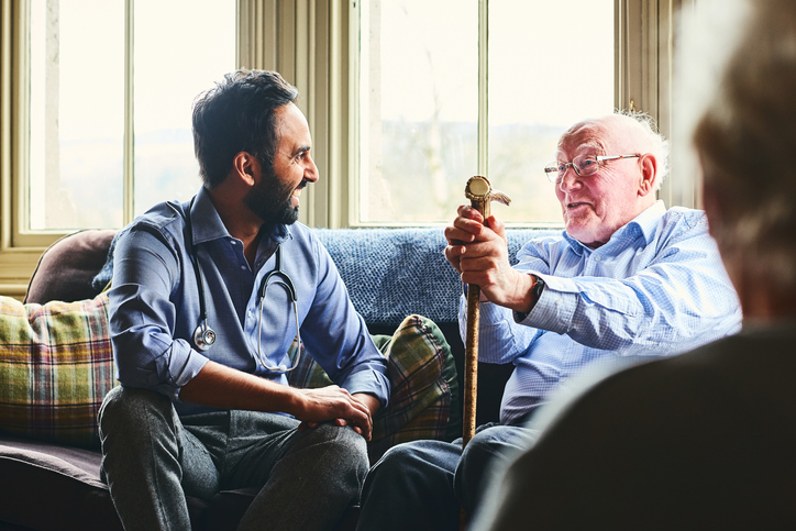 seated senior man with cane smiles and talks with his adult son, seated next to him