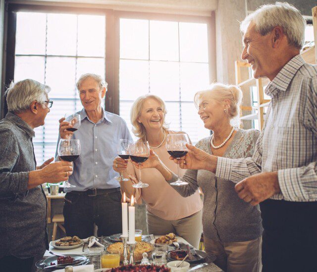 Group of close-knit senior friends smile and toast wine together during a social celebration