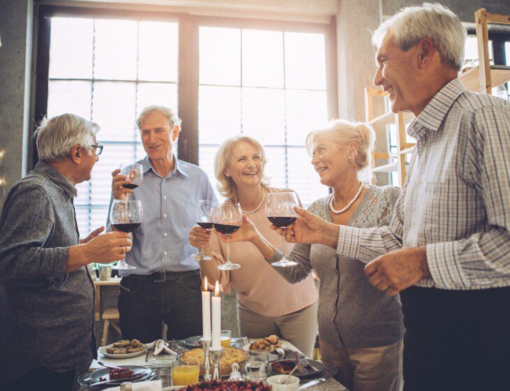 Group of close-knit senior friends smile and toast wine together during a social celebration