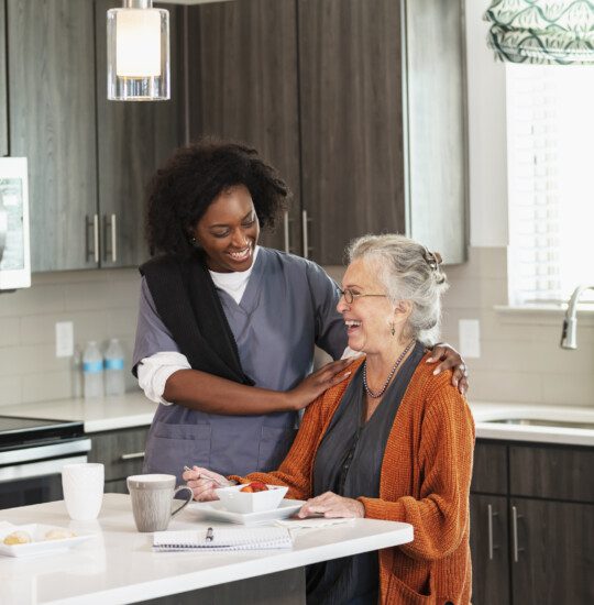 senior woman smiles at her home care nurse while enjoying lunch in the kitchen