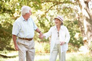 happy senior couple hold hands and walk along a tree-lined garden path in the summer