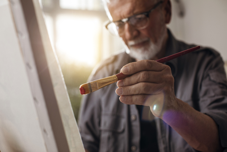 close-up of senior man with glasses painting a canvas