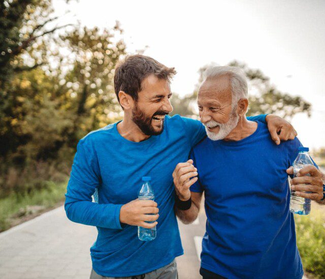 senior man and his adult son laugh together, drinking water after a run