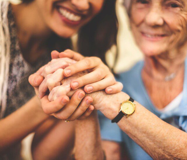 close-up of senior woman and her adult daughter smiling and holding hands