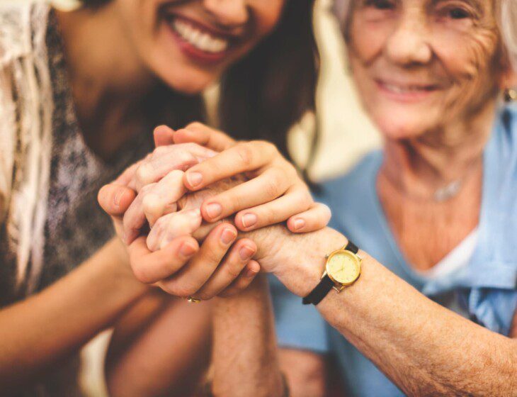 close-up of senior woman and her adult daughter smiling and holding hands