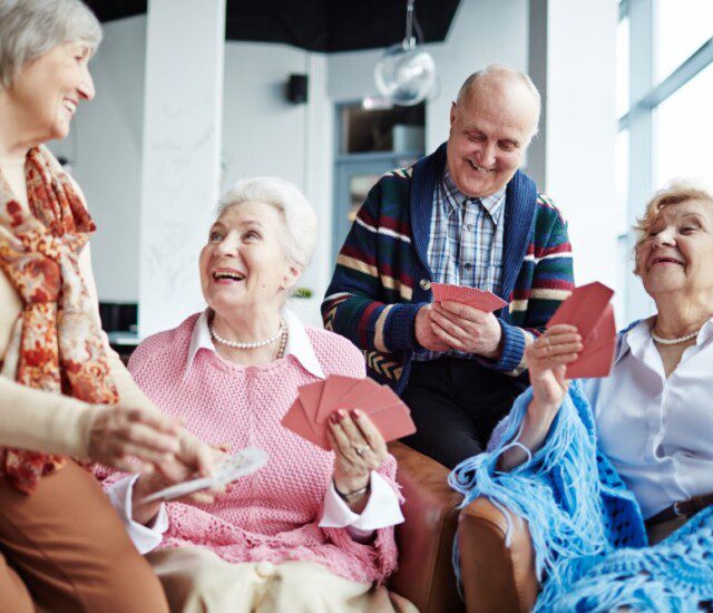 group of joyful senior friends smile while playing a card game together