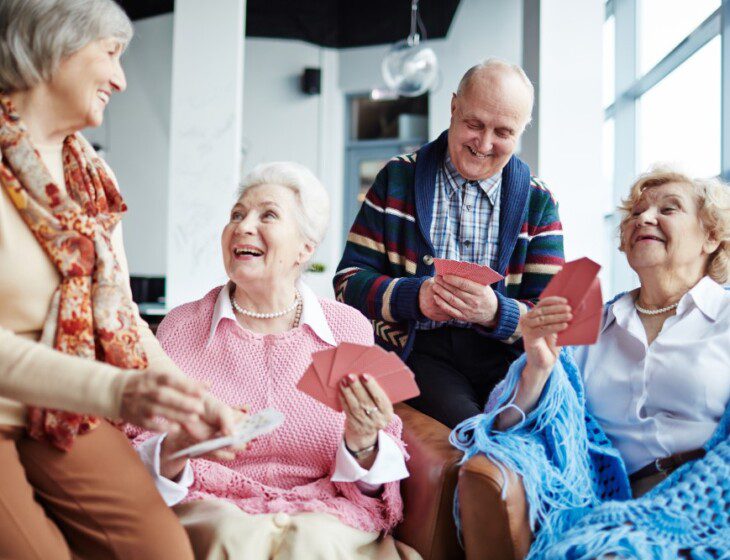 group of joyful senior friends smile while playing a card game together