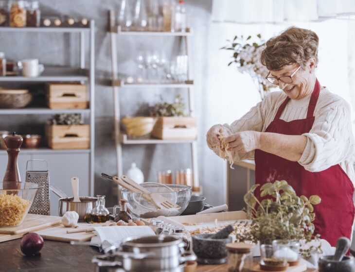 cheerful senior woman in red apron cooks a holiday meal in her contemporary kitchen