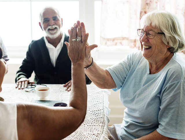 two senior women smile and high-five after winning a board game with friends