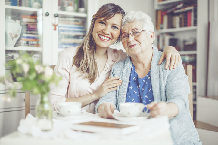senior woman and her adult daughter smile and lean close for a picture while seated and having tea