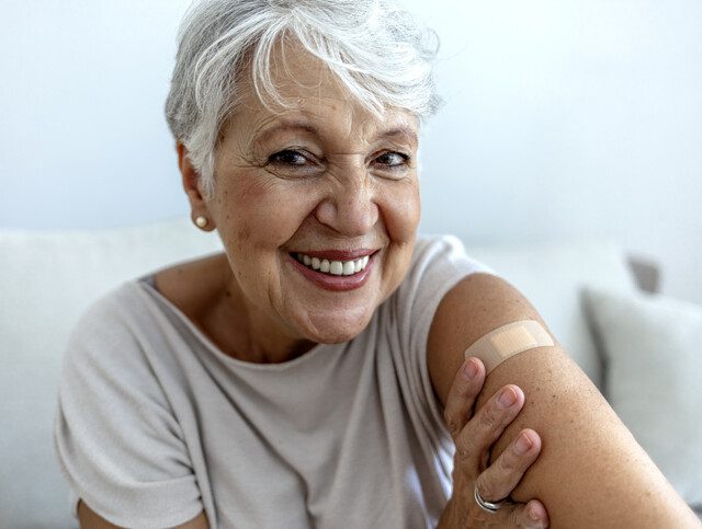 senior woman smiles and shows off her band aid, placed on her arm where she received her vaccine