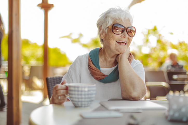 senior woman with fashionable sunglasses holds large coffee cup while seated outdoors, smiling at her companion
