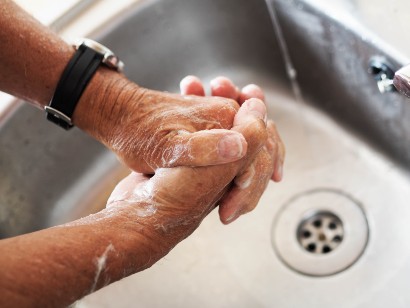 senior washing their hands with soap and water in a sink