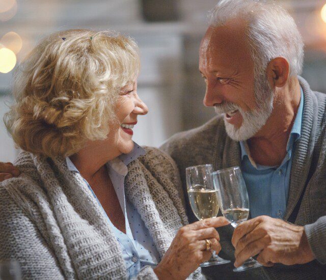 senior couple looks lovingly at each other while toasting champagne glasses for New Years