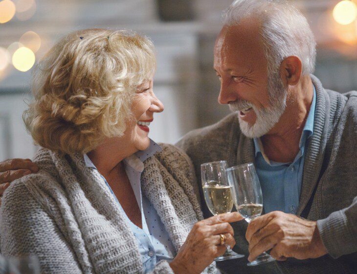 senior couple looks lovingly at each other while toasting champagne glasses for New Years